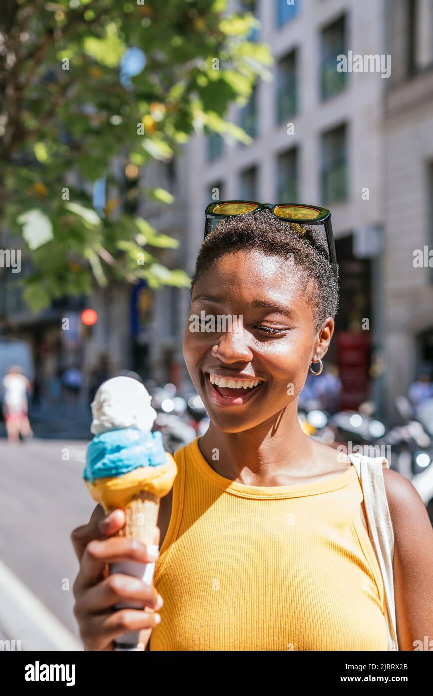 cheerful african american woman smiling while looking to her ice-cream. She is in the street on a summer day Stock Photo