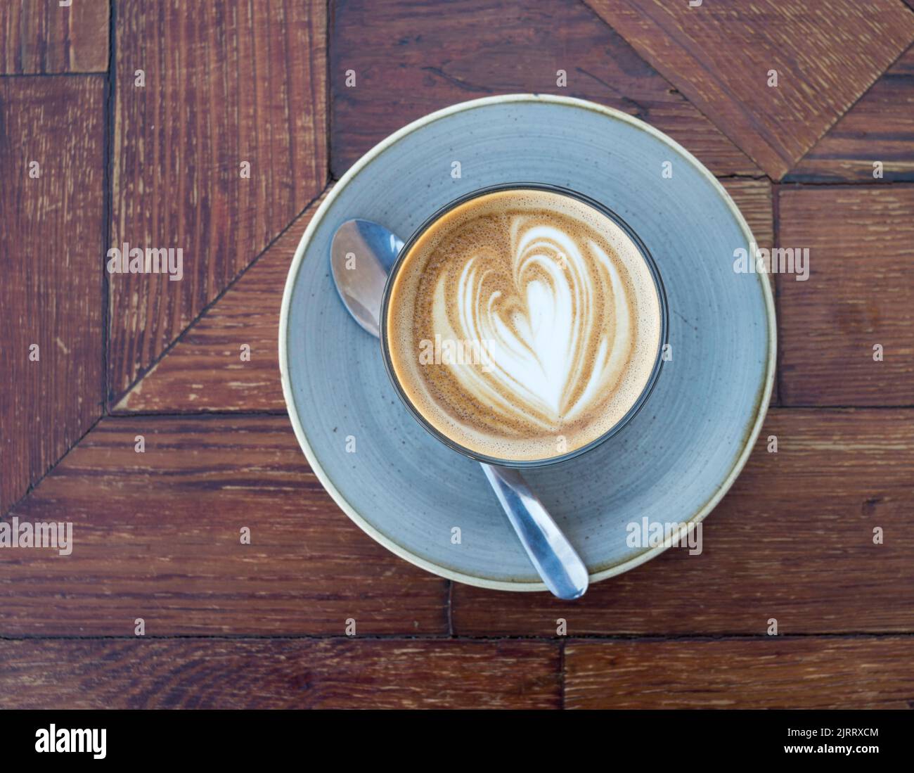 A cup of flat white coffee with saucer and spoon against a dark wood background Stock Photo