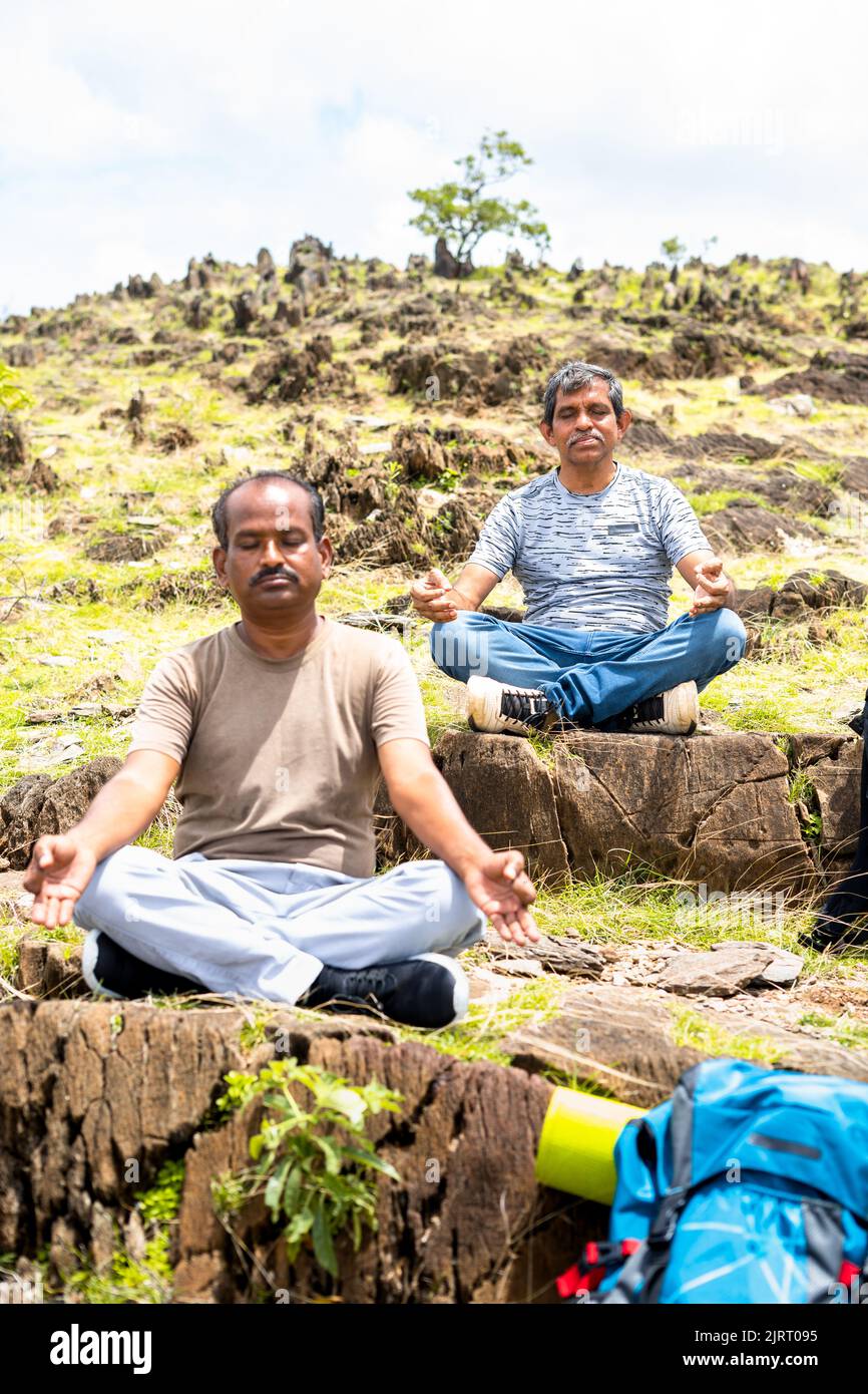 handheld shot of Two Middle aged hikers with eyes closed doing meditation on top of hill during morning - concpet of mindfulness, self care and Stock Photo
