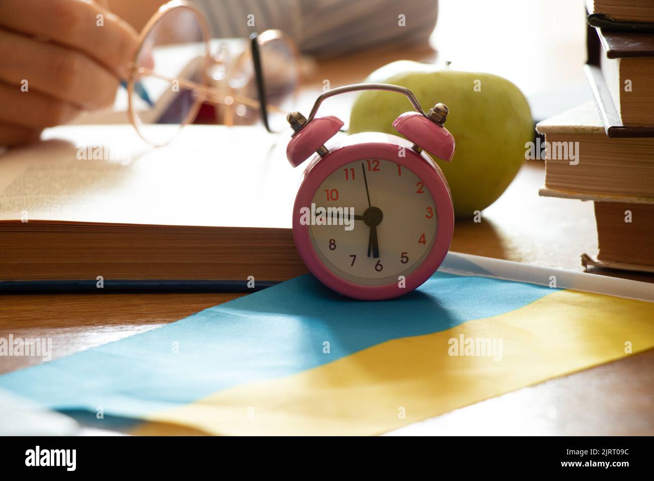 An alarm clock stands on a table near books and an apple on the flags of Ukraine, school education in Ukraine, time to study, education in Ukraine Stock Photo