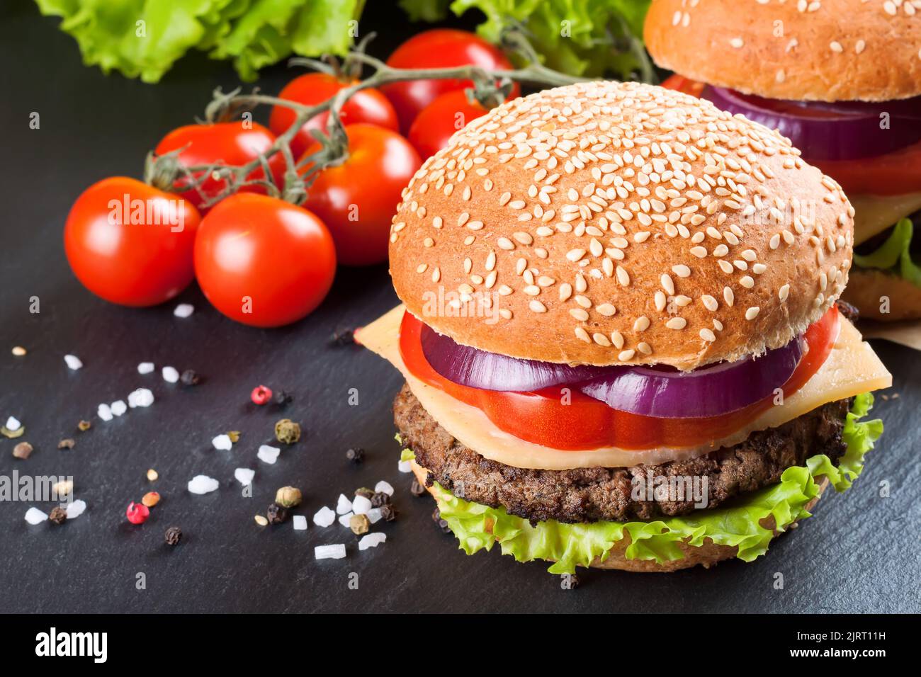 Homemade cheeseburger with beef patties, fresh salad, tomatoes and onion on seasame buns, served