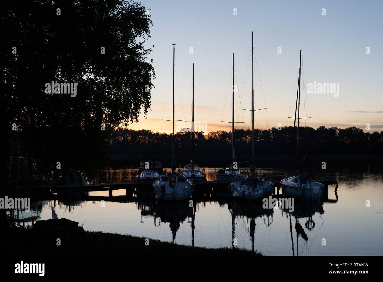 The sky and boats reflected on the water with trees in the background ...