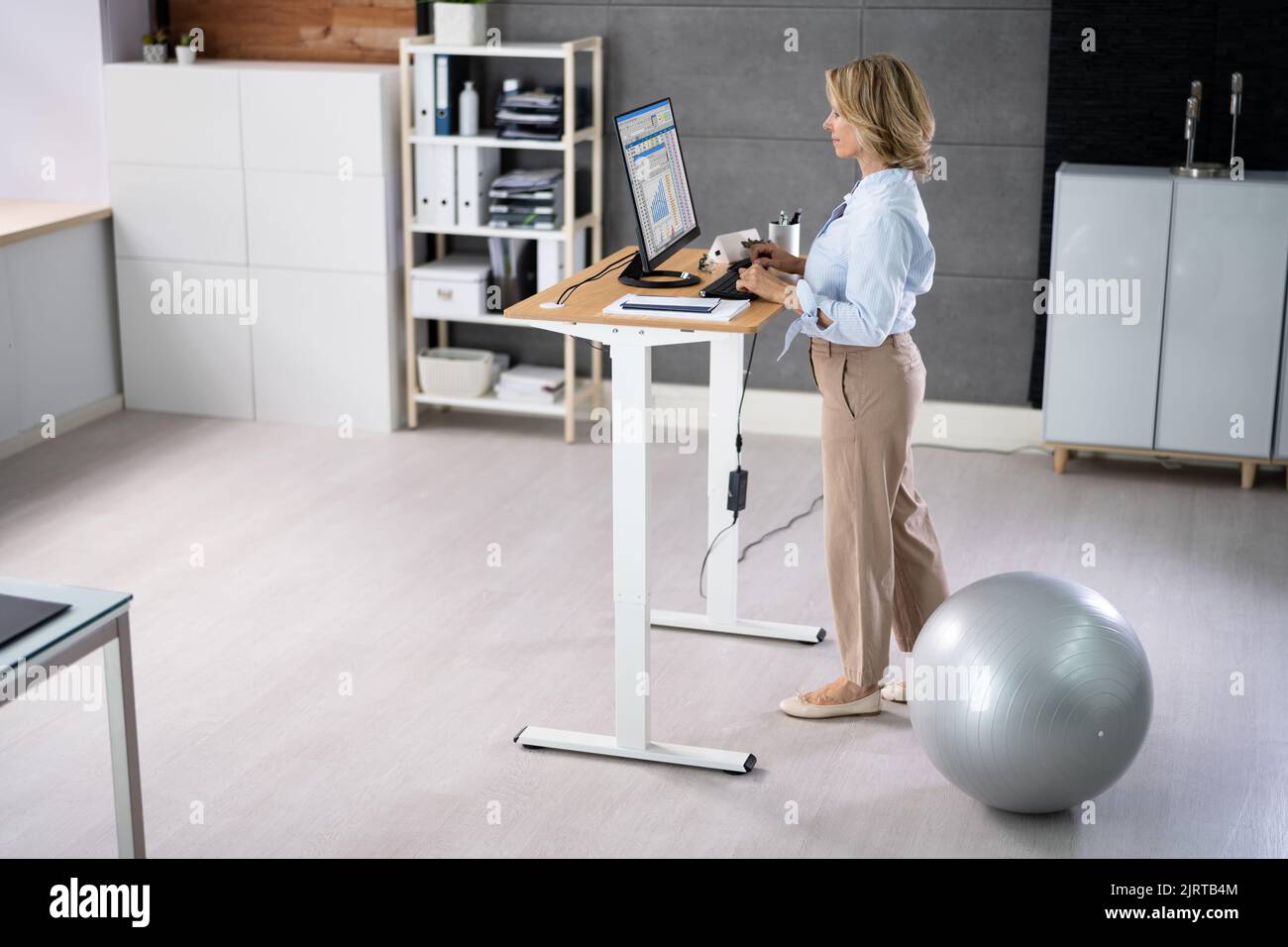 Woman Using Adjustable Height Standing Desk In Office For Good Posture