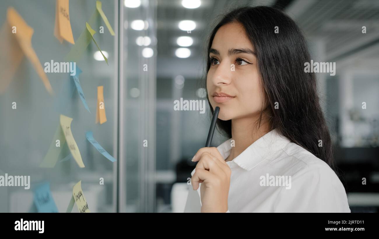 Arabian business lady managing daily tasks stand near board in office write reminder information instruction on paper sticky notes read stickers Stock Photo