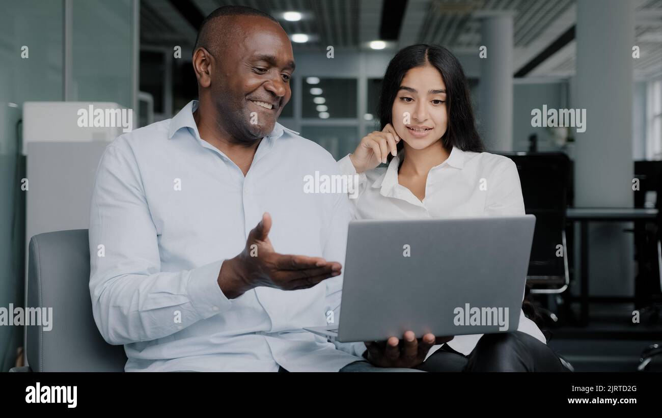 Diverse colleagues two business partners african arabian co-workers discuss internet project on laptop at office meeting planning working main tasks Stock Photo