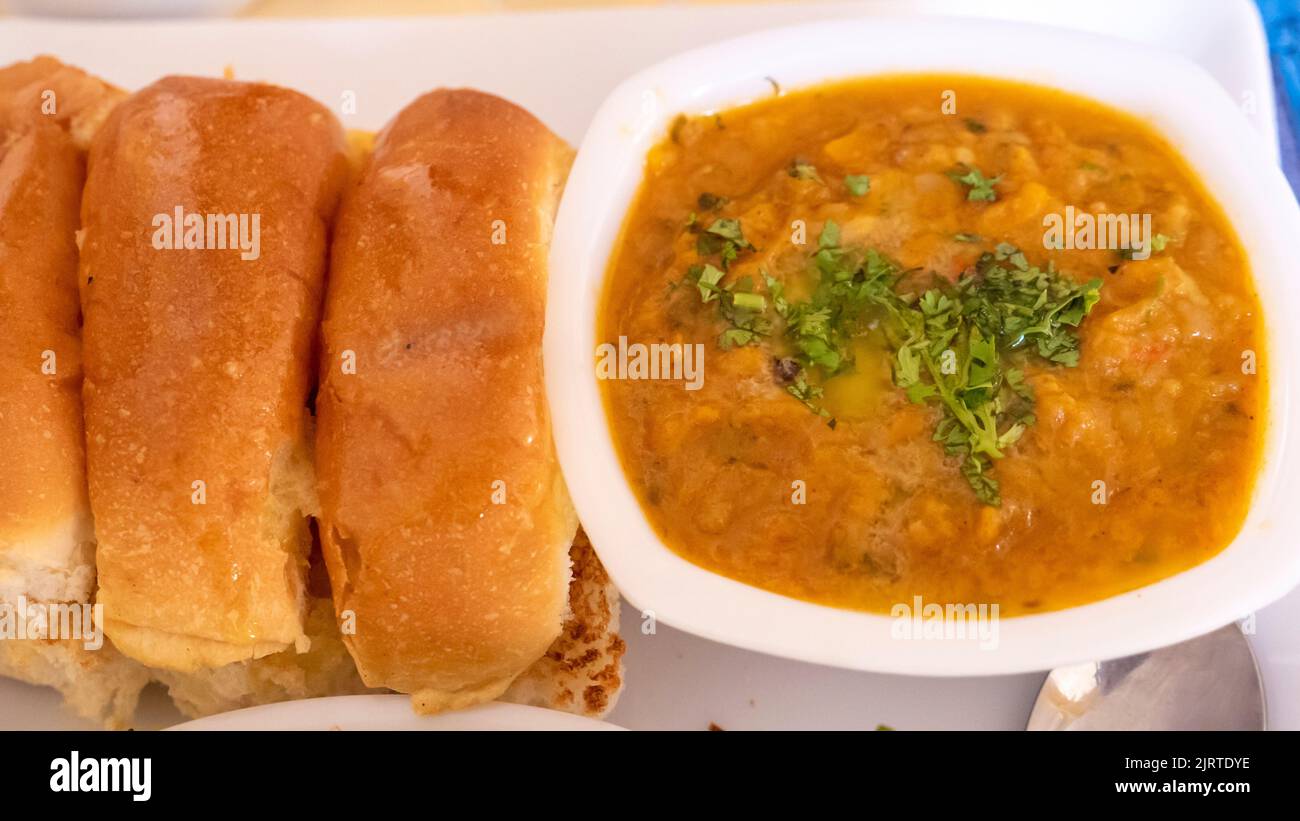 Pav bhaji fast food dish from India. Consists of a thick vegetable curry served with a soft bread roll, served in a plate. Stock Photo