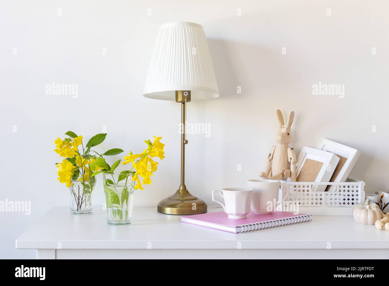 White floor lamp with lampshade. A pink notebook with springs, a white coffee mug, a wooden toy bunny on hinges, sitting on a plastic box. Dresser. Mi Stock Photo