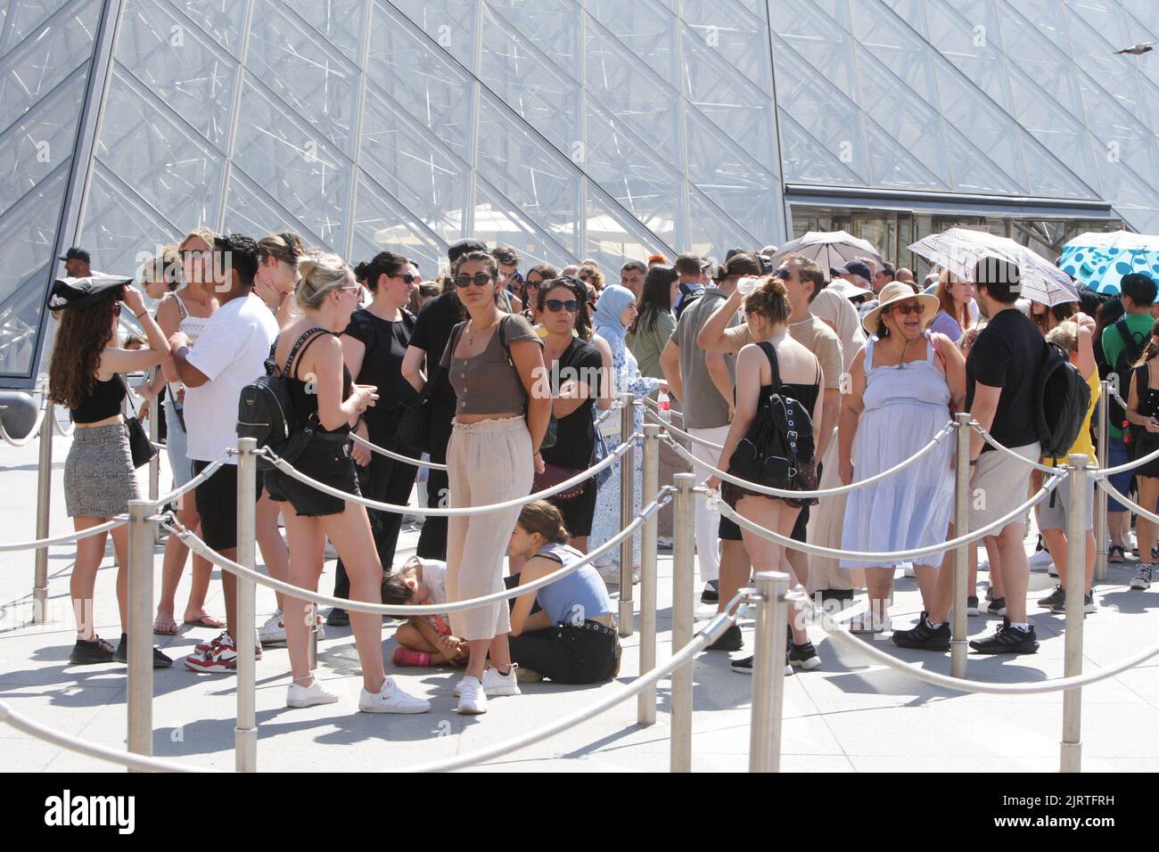 People wait line up near Pyramid at the Louvre Museum during a hot