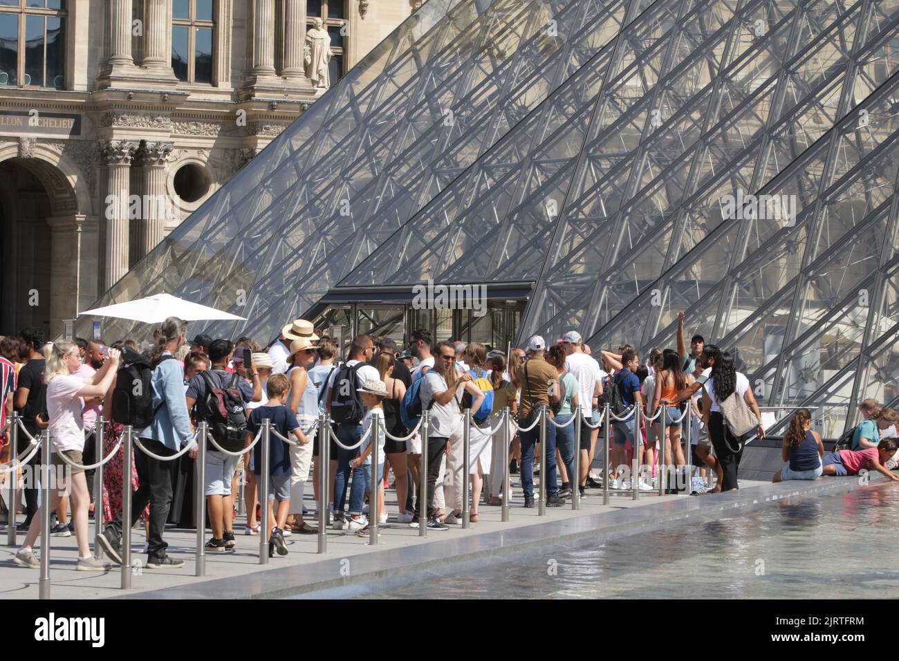 People wait line up near Pyramid at the Louvre Museum during a hot