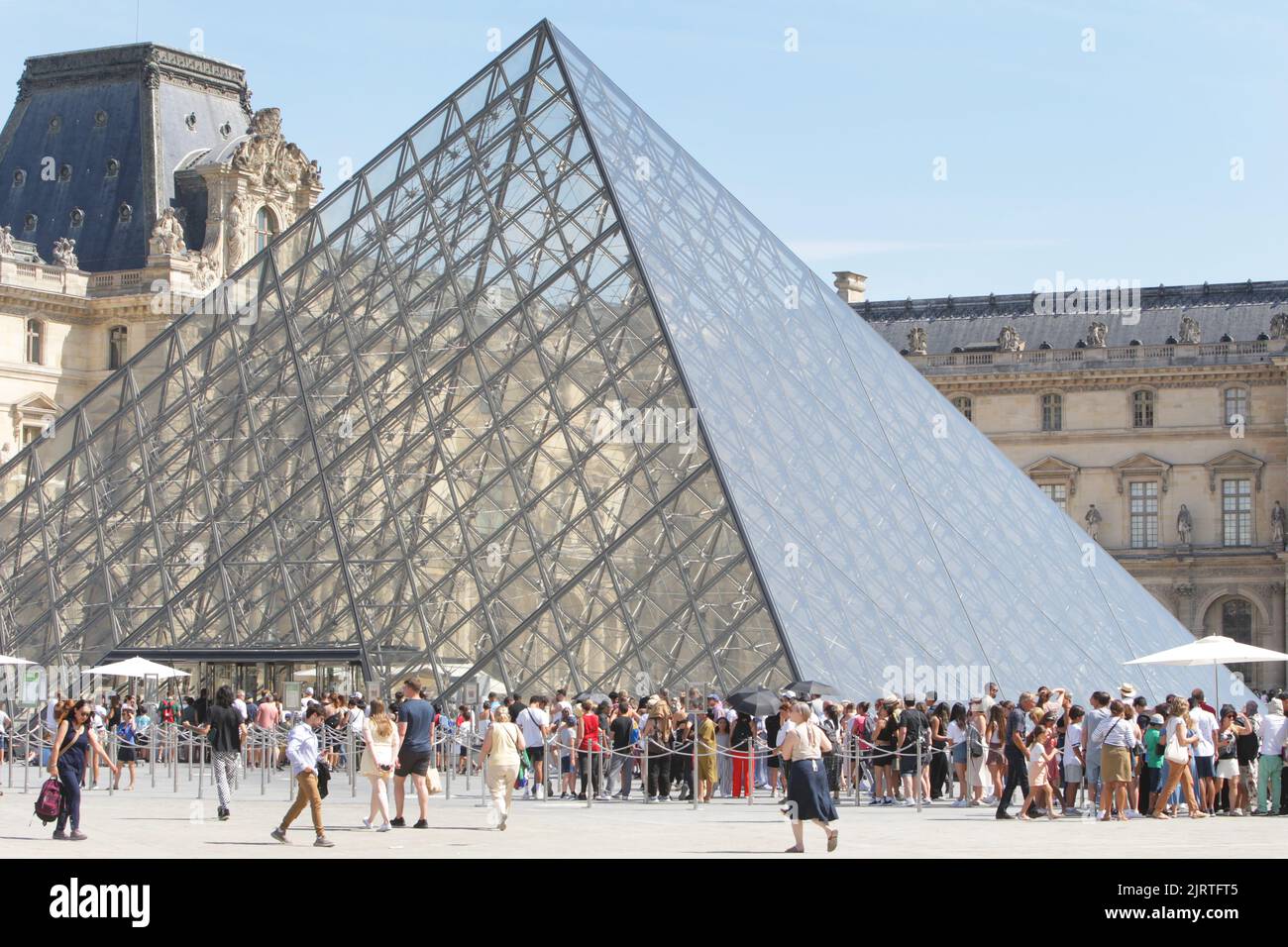 People wait line up near Pyramid at the Louvre Museum during a hot