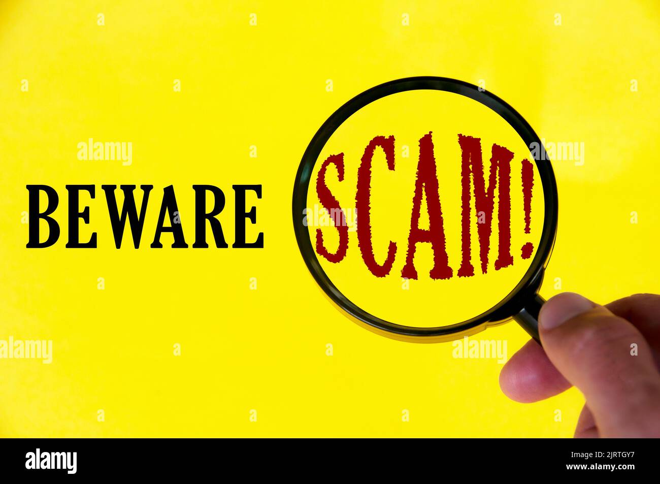 Beware scam text on yellow cover with hand holding magnifying glass. Scamming and fraud concept. Stock Photo