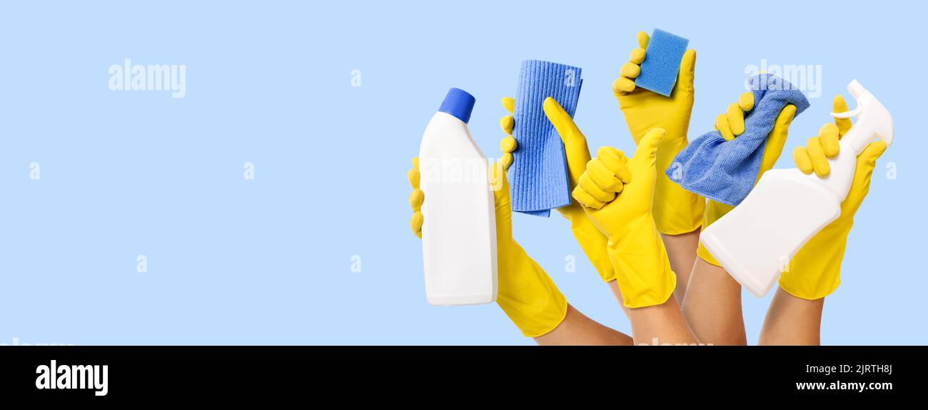 hand with yellow rubber glove holding cleaning supplies on blue background. banner with copy space Stock Photo