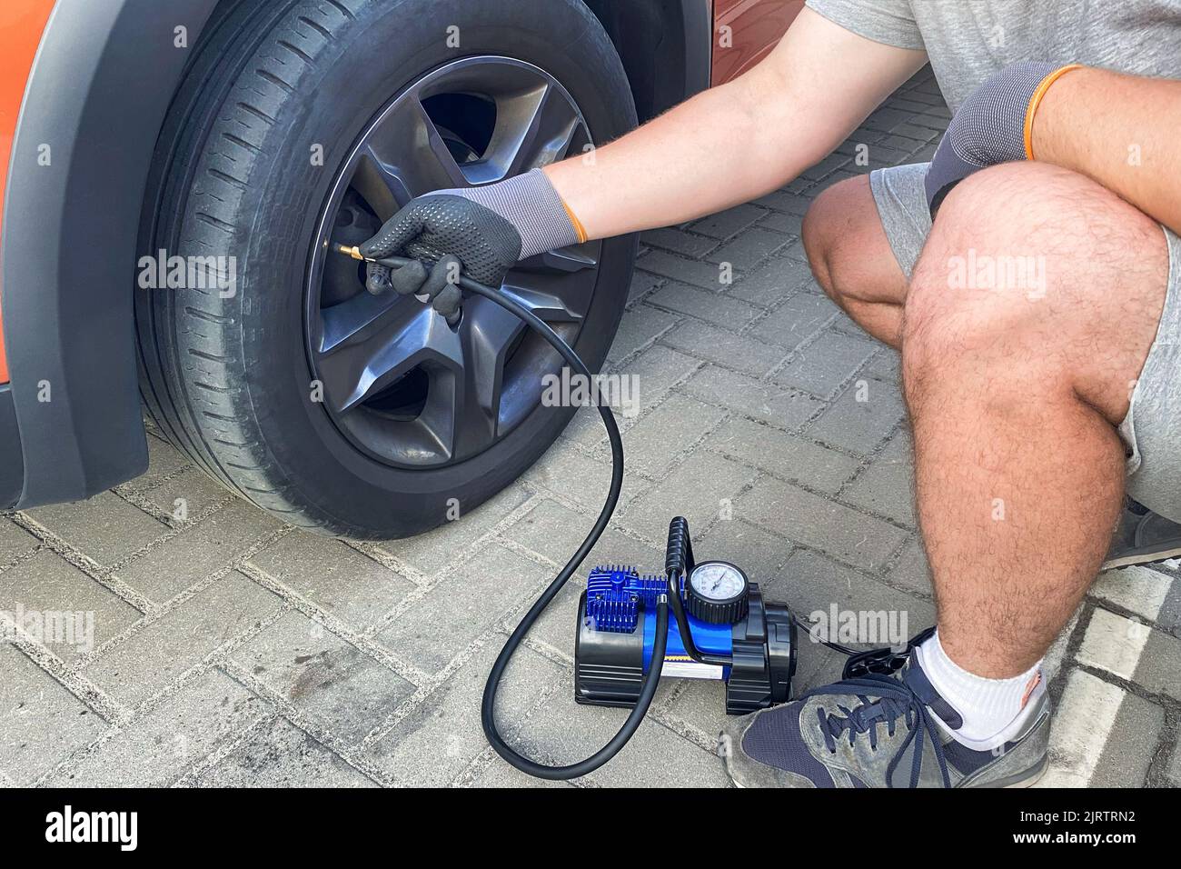 Car service. Male hand in gloves checks pressure in car tires in sunny day. Stock Photo