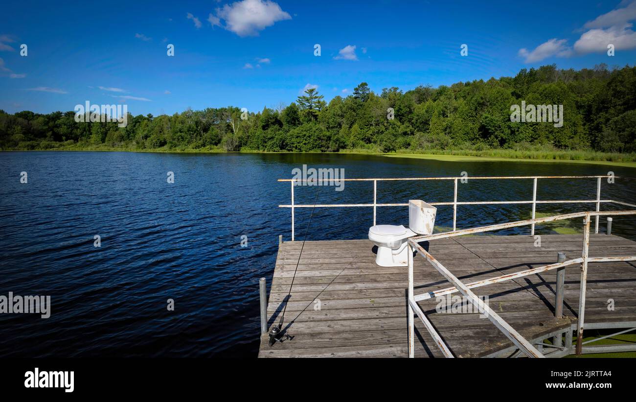 A fishing pole and toilet sit on a wooden pier on Gass Lake near Manitowoc, Wisconsin. Stock Photo