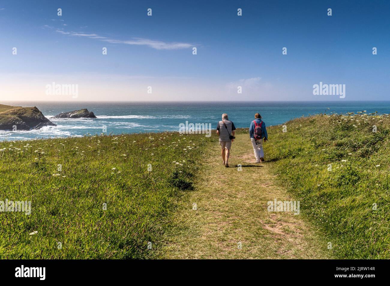 Mature holidaymakers walking along a footpath on the coast of West Pentire in Newquay in Cornwall in the UK.The spectacular beautiful poppy fields ove Stock Photo