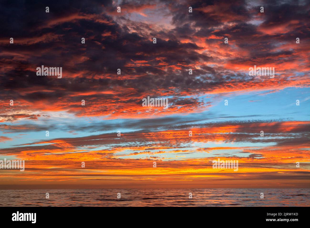 A beautiful and unusual sunset with dark clouds mixed with bright orange hints of sunlight over the Pacific ocean. Stock Photo