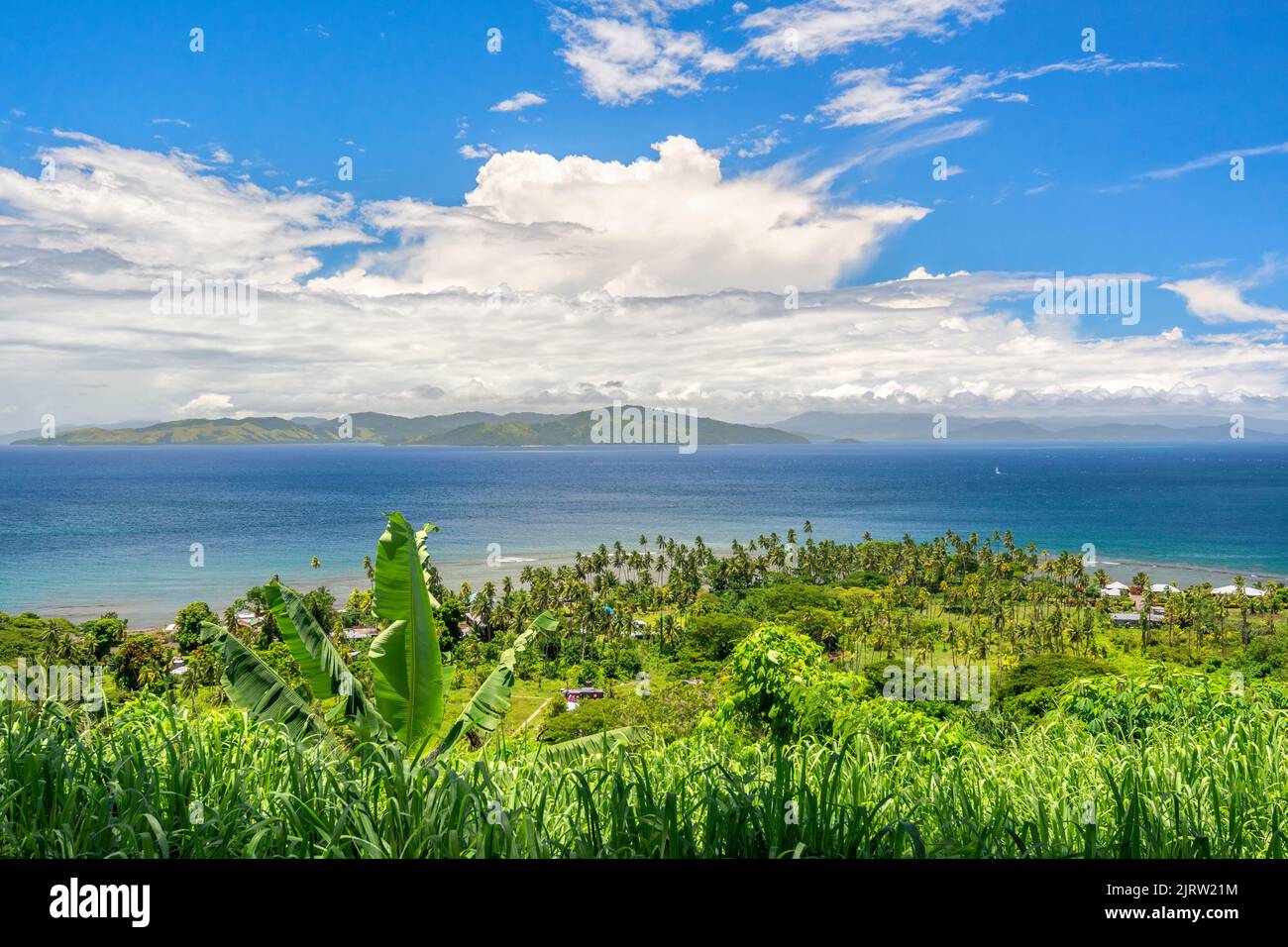 Cliffside overlook from a lush, tropical viewpoint shows the beautiful blue sky and water surrounded by green foliage. Stock Photo