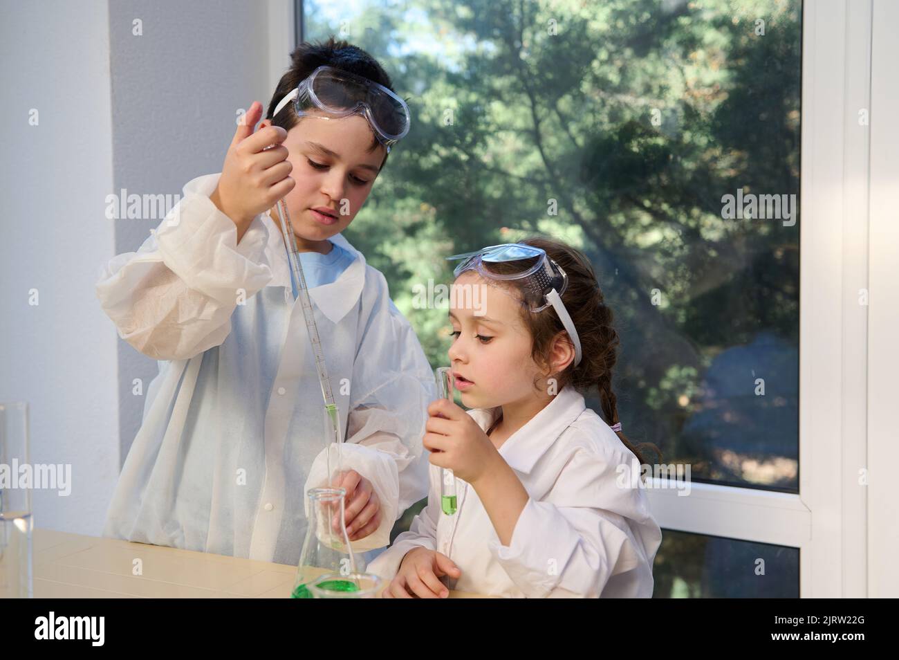 Adorable children, boy and girl in white lab coats and safety goggles, making science