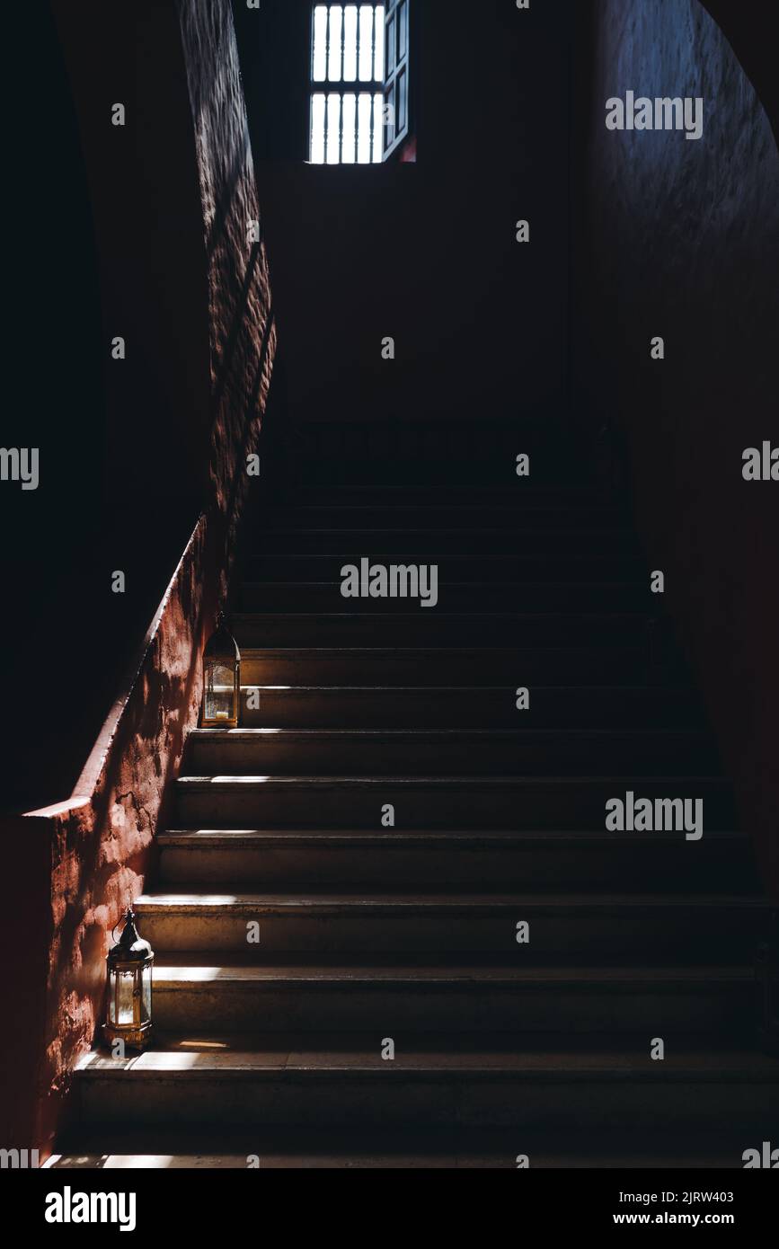 A vertical shot of a dark staircase slightly lit by light from a window. Stock Photo