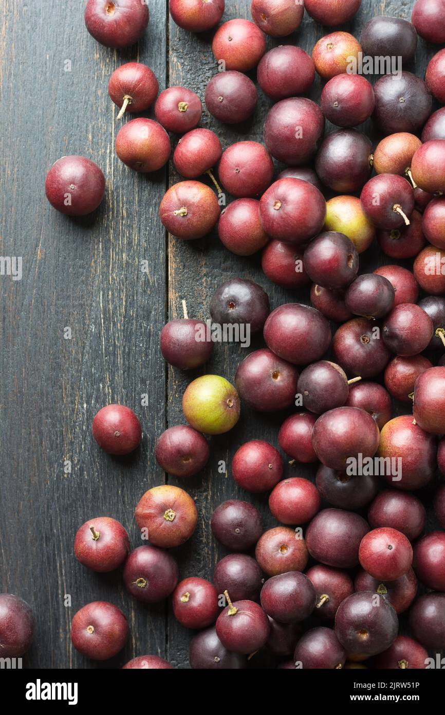 scattered governor's plum fruits on a black rustic table top, flacourtia indica, also known as ramontchi, madagascar plum or indian plum Stock Photo