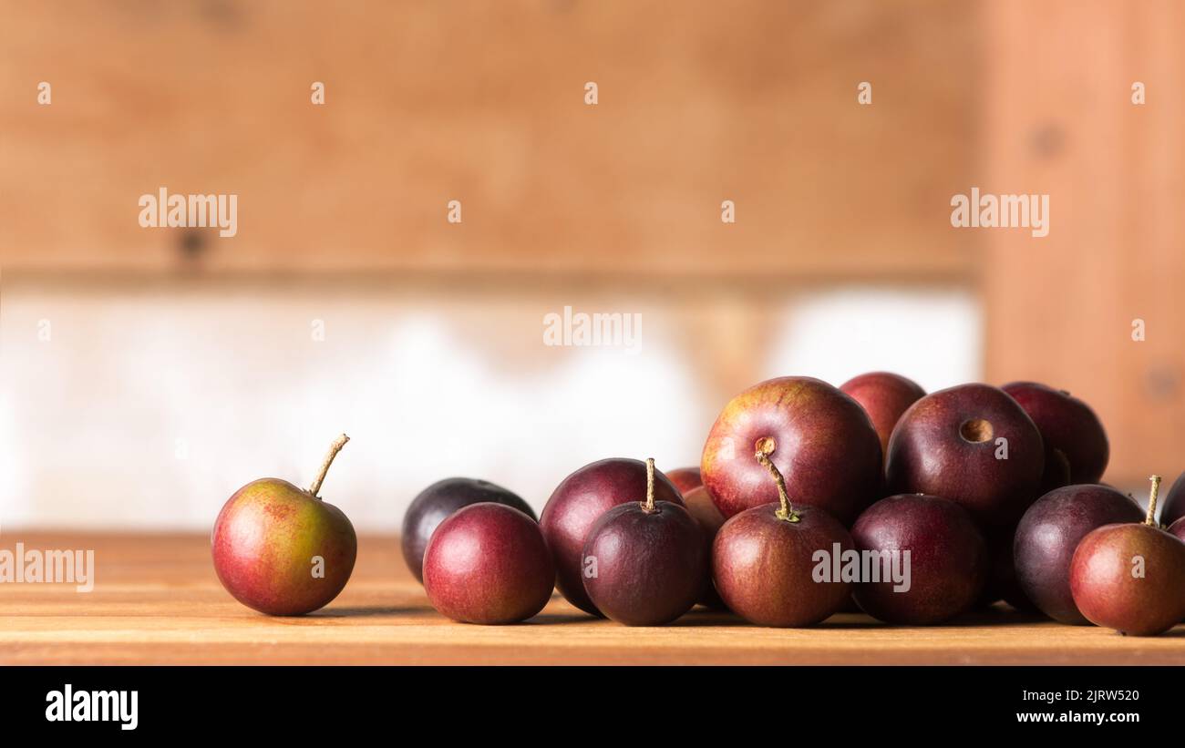 close-up of governor's plum fruits on wooden table top, flacourtia indica, also known as ramontchi, madagascar plum or indian plum, reddish black Stock Photo