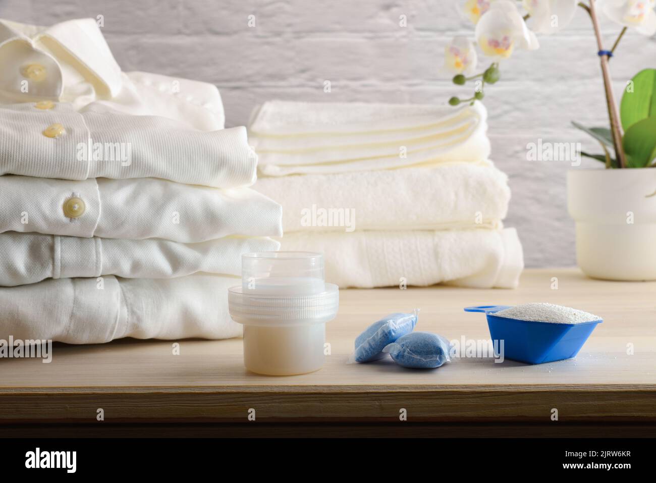 Different types of laundry detergents on wooden table with freshly washed folded white clothes. Front view. Horizontal composition. Stock Photo