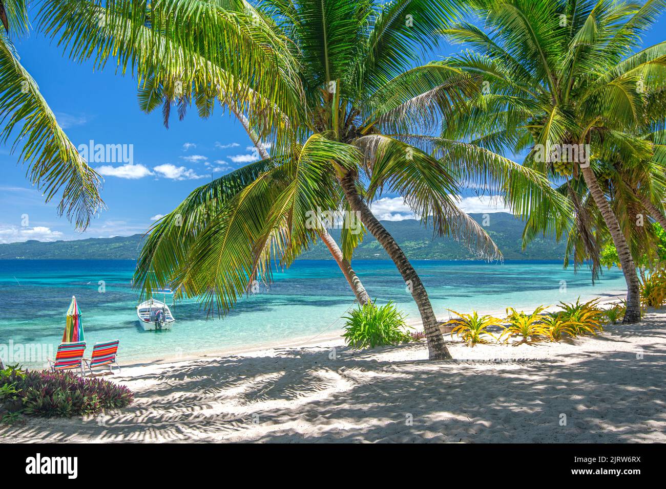 A classic view of a tropical beachfront resort in the south pacific showing plenty of sunshine, blue water and vibrant skies. Stock Photo