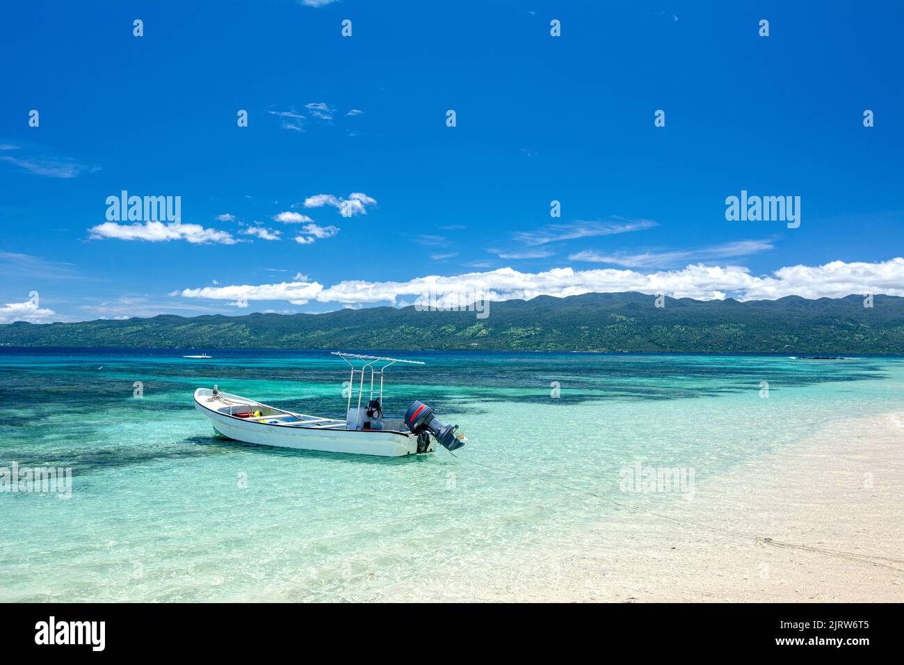 Classic view of a tropical beach scene with a floating boat in crystal clear water and a white sandy shoreline. Stock Photo