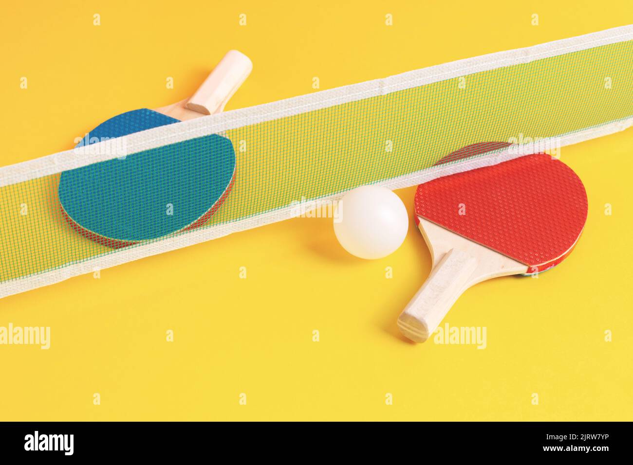 Red and blue table tennis rackets, white ball and net on yellow
