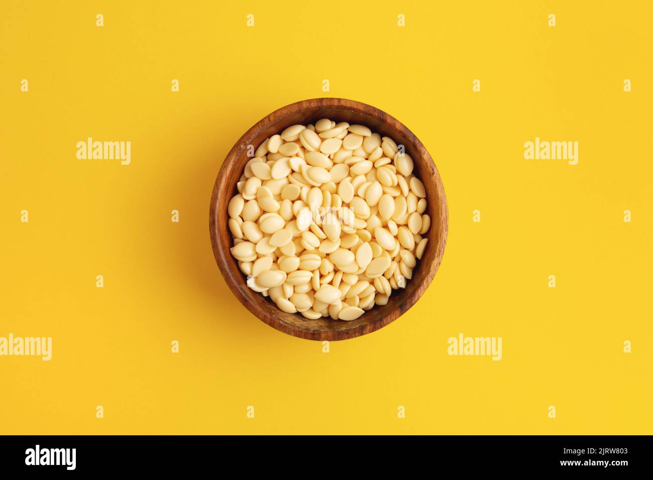 Depilatory film wax bean granules in a wooden bowl on yellow background. Cosmetics, hair removal. Stock Photo