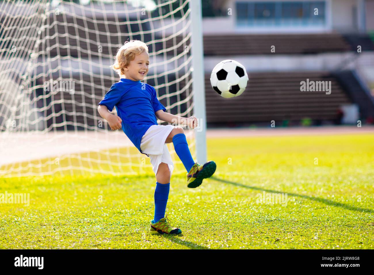 Kids play football on outdoor stadium field. Children score a goal