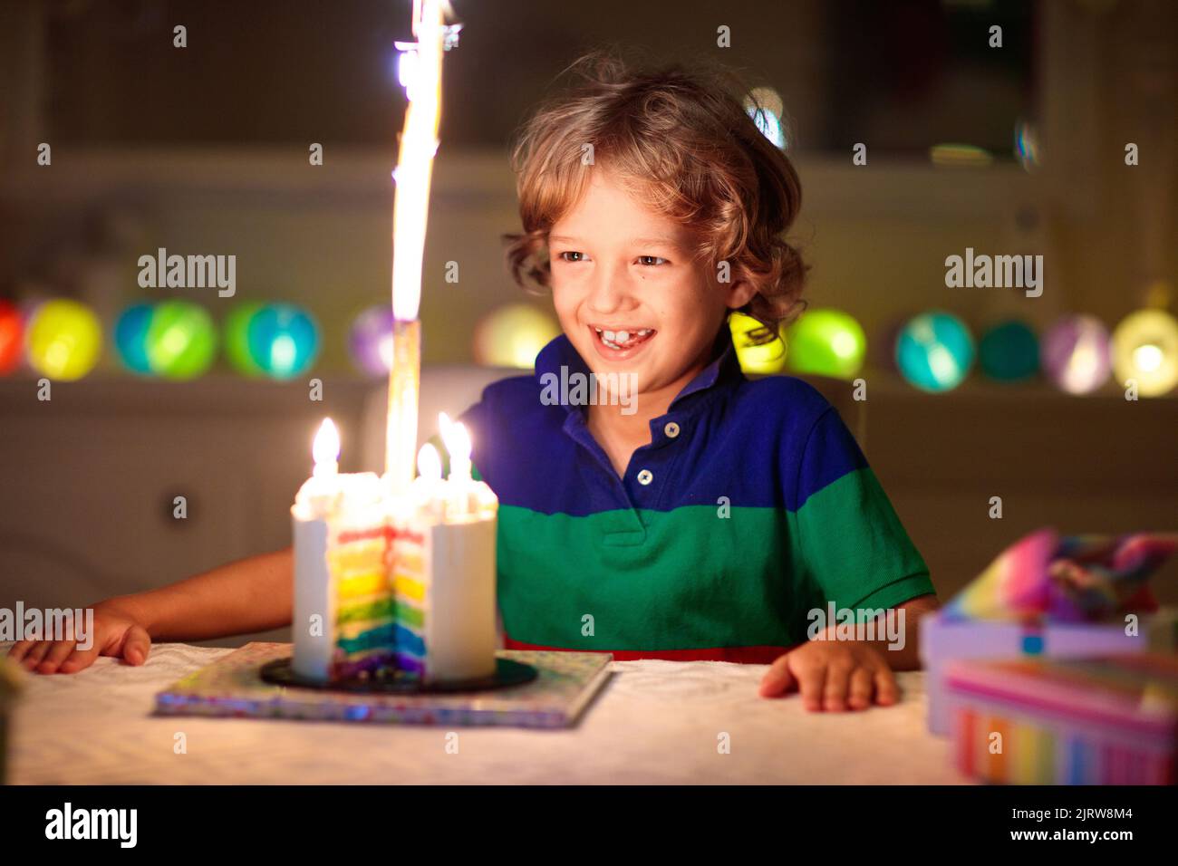 Kids birthday party. Child blowing candles on cake and opening presents