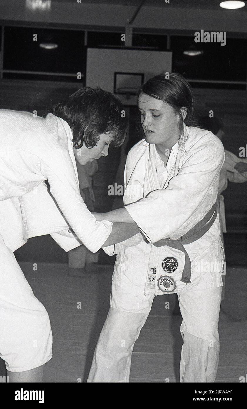 1970s, two teenage female judo competitors in combat, with their hands and arms locked in a hold position in this martial art, England, UK. Badges on one of the jackets, British Judo Association and Downs. Created in 1882 by Dr Jigoro Kano, a Japanese educationalist as a derivity of a martial art, Judo does not use striking or training weapons as other martial arts, with it's emphasis on grappling, with throwing and groundwork. Introduced to the UK in 1918, the British Judo Association was formed in 1948. Stock Photo