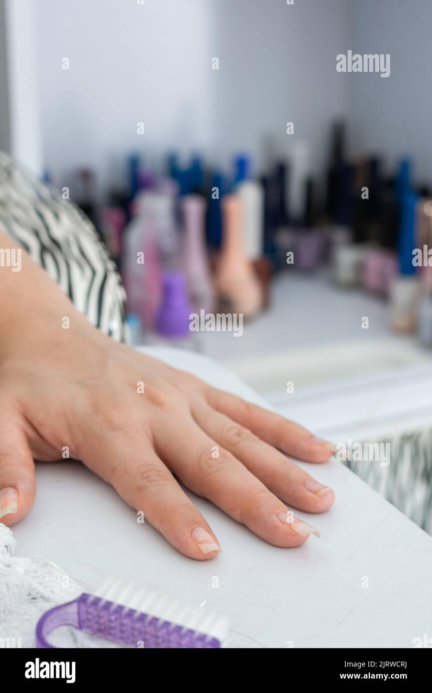 detail of latin girl's hand, placed on the manicure table, ready to start painting and decorating the nails. in the background many colored nail polis Stock Photo