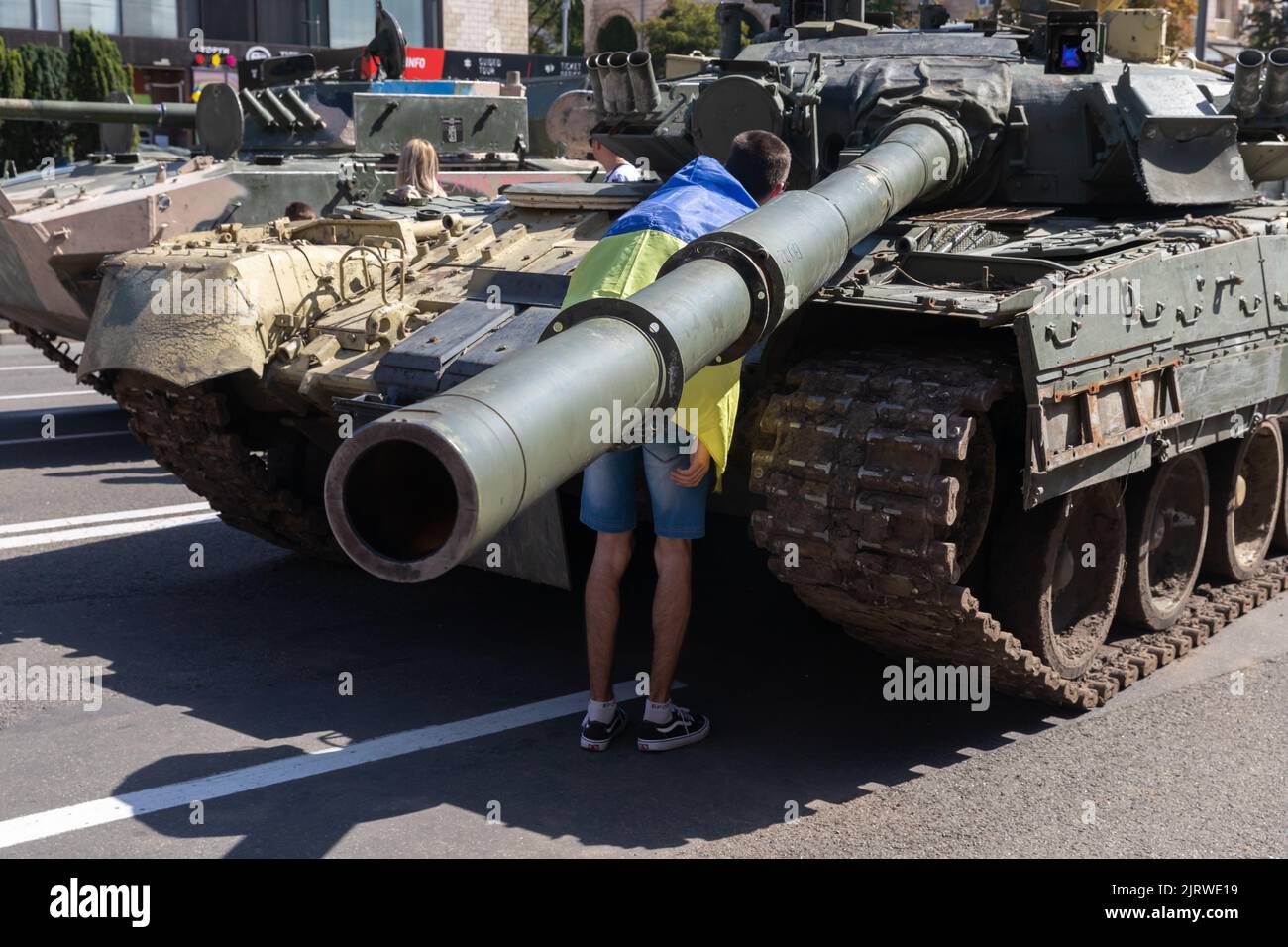 A man wrapped with a Ukrainian flag looks at a destroyed Russian tank. An exhibition of destroyed Russian equipment is being organized at Khreshchatyk. Six months ago, Russian military troops were deployed by Russian president Vladimir Putin to invade Ukraine. He reportedly reckoned that they would capture Kyiv in three days, Stock Photo