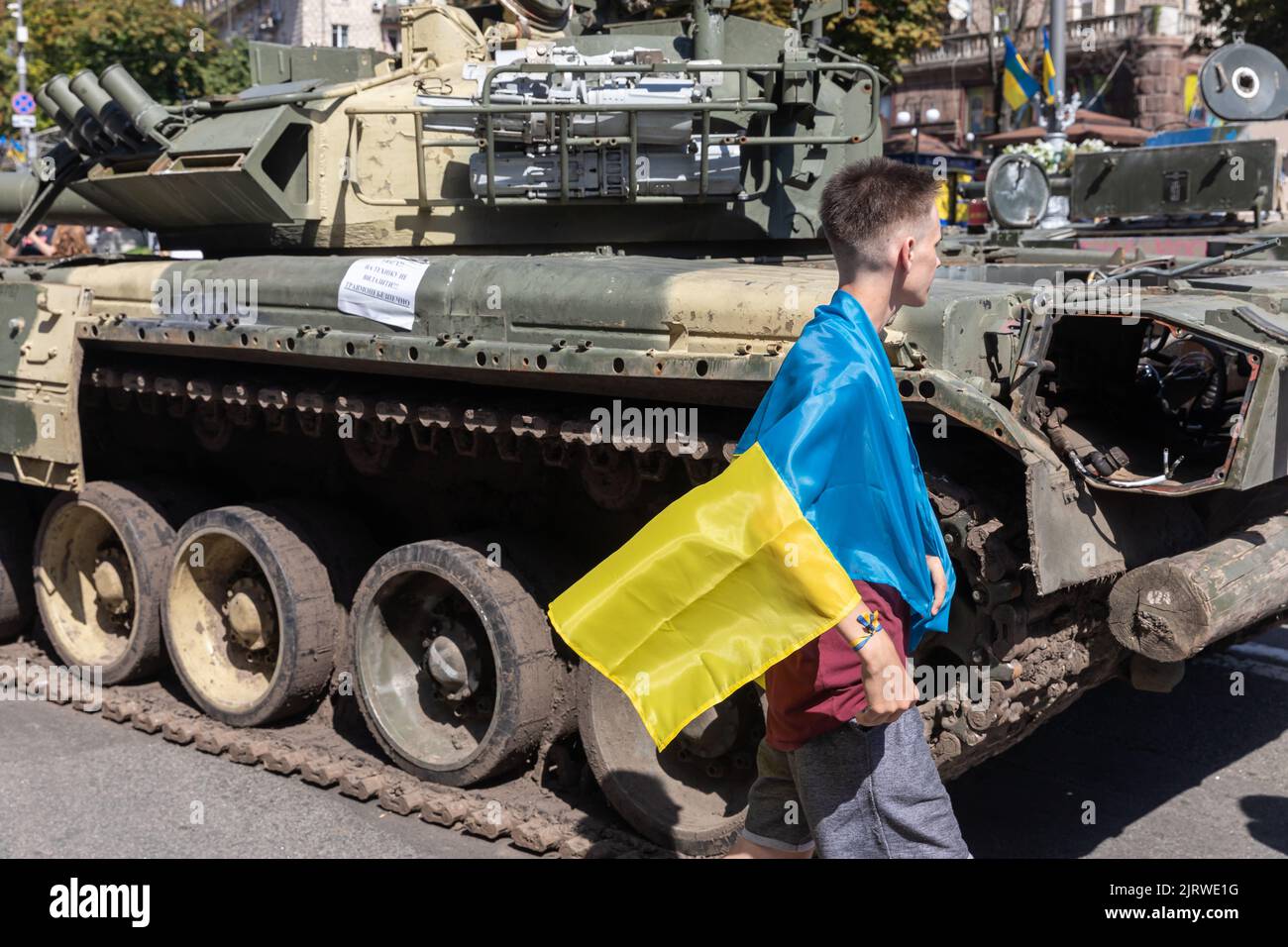 A man wrapped with a Ukrainian flag looks at a destroyed Russian tank. An exhibition of destroyed Russian equipment is being organized at Khreshchatyk. Six months ago, Russian military troops were deployed by Russian president Vladimir Putin to invade Ukraine. He reportedly reckoned that they would capture Kyiv in three days, Stock Photo