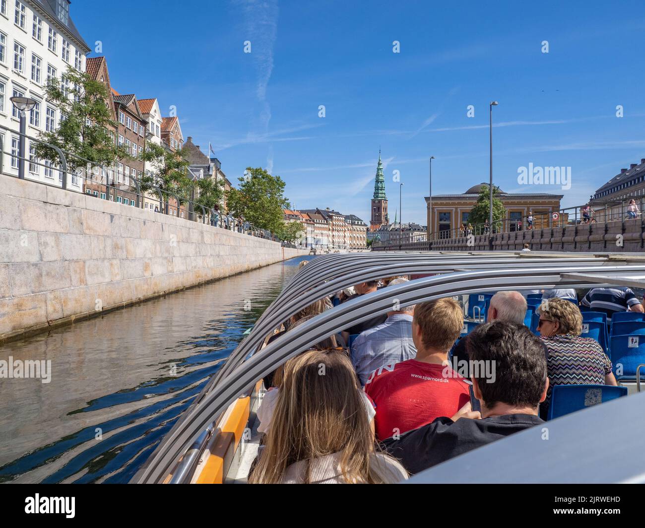 Tourists enjoying a guided tour of Copenhagen Denmark on a canal boat sailing along the Frederiksholms Kanal in bright sunshine Stock Photo