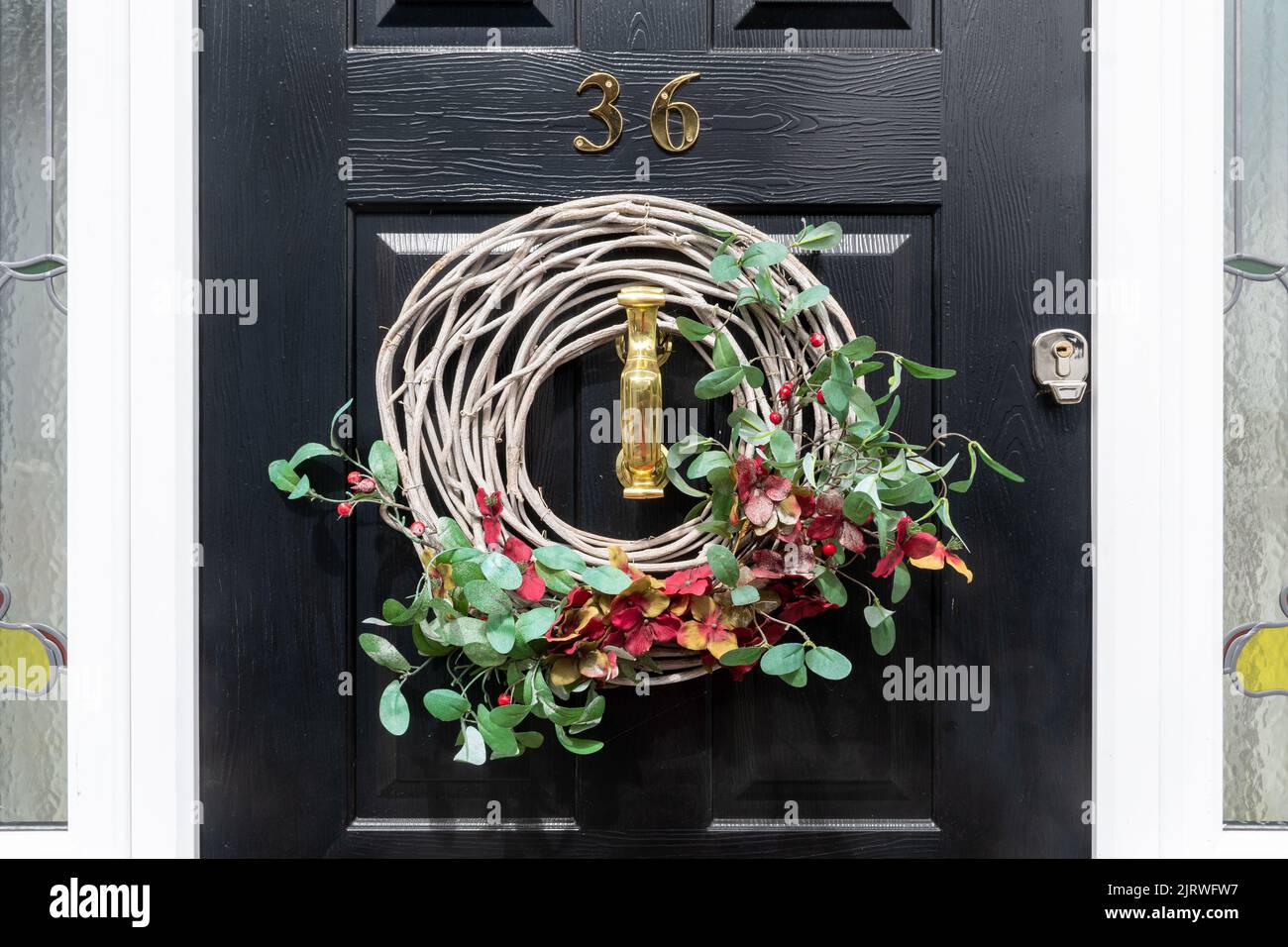 Wreath on front door with red flowers and green leaves or foliage, decorative wreath Stock Photo