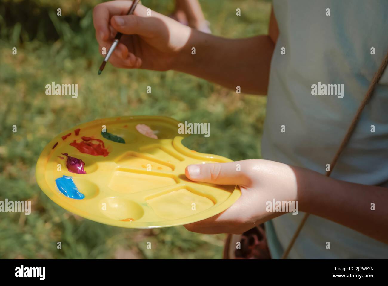 Child girl holding palette with paints and brush for painting outdoors Stock Photo