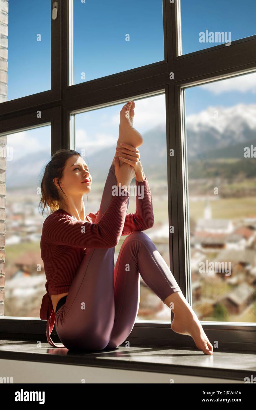 woman doing yoga exercise on window sill at studio Stock Photo