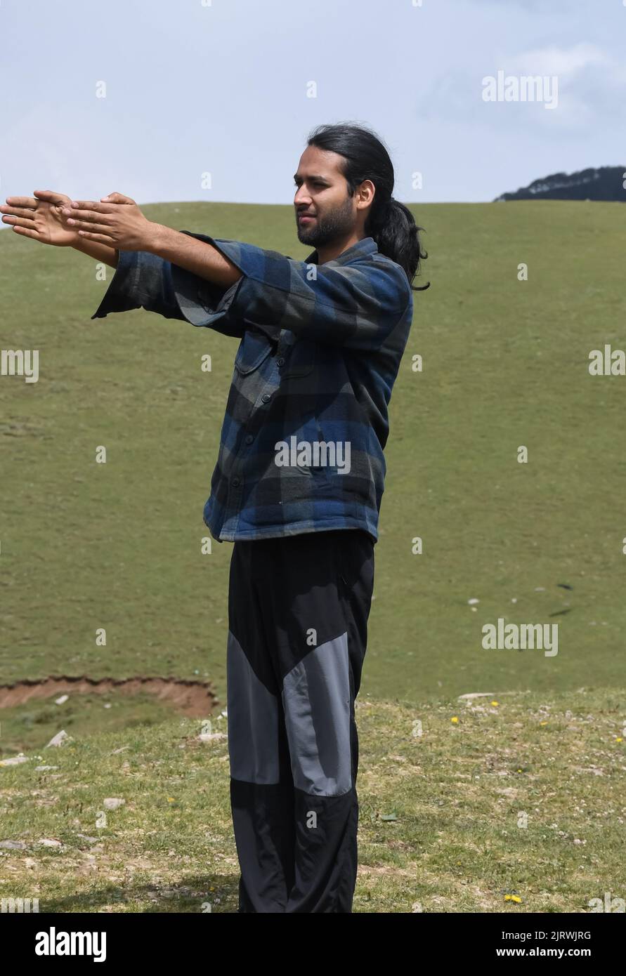 A young Indian guy warm up his body with doing Front Arm Raise exercise in the mountain. Stock Photo