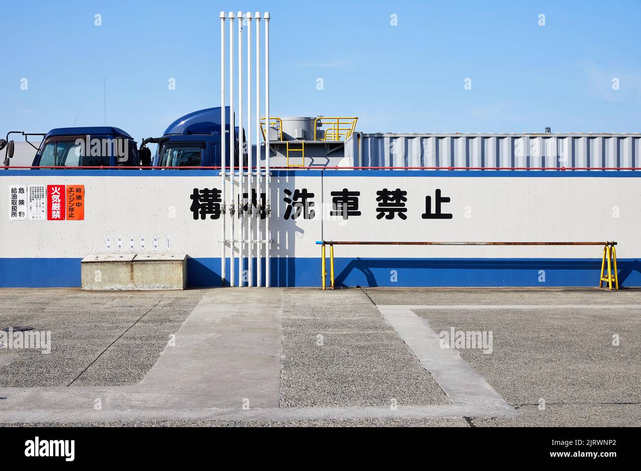 Trucks behind wall with Japanese text; Kawasaki, Kanagawa Prefecture, Japan Stock Photo