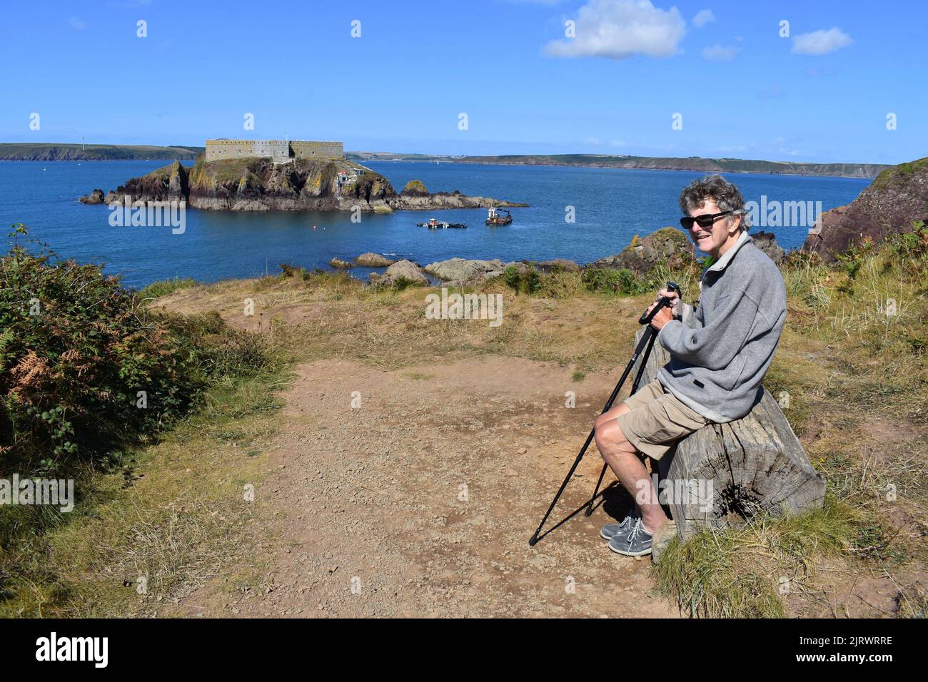Walker enjoying a rest on the Pembrokeshire coastal path with a view of Thorne island and across Milford Haven waterway, Angle, Pembrokeshire, Wales Stock Photo