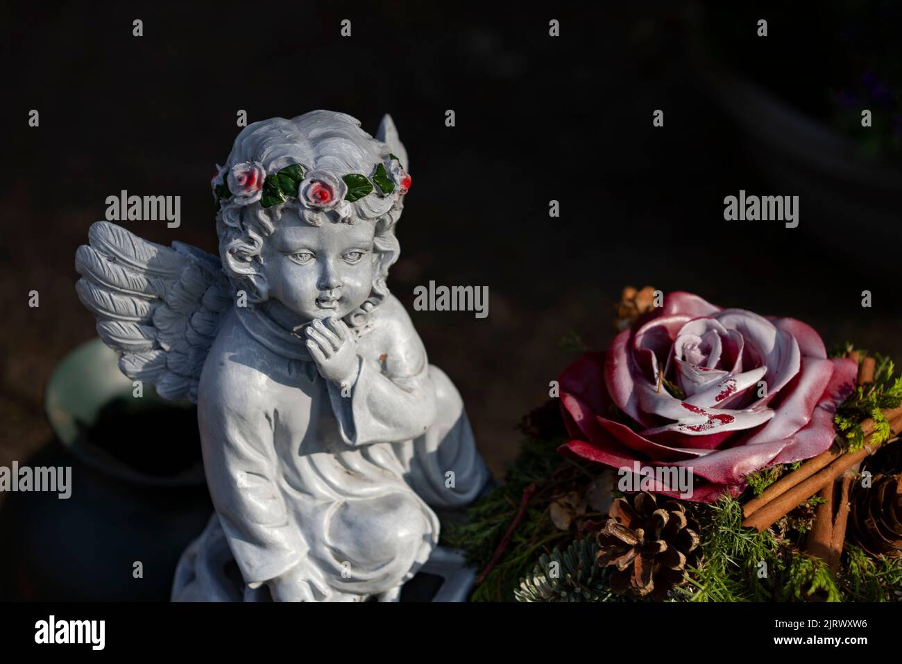 A cute little angel statue with a floral wreath near a rose figurine