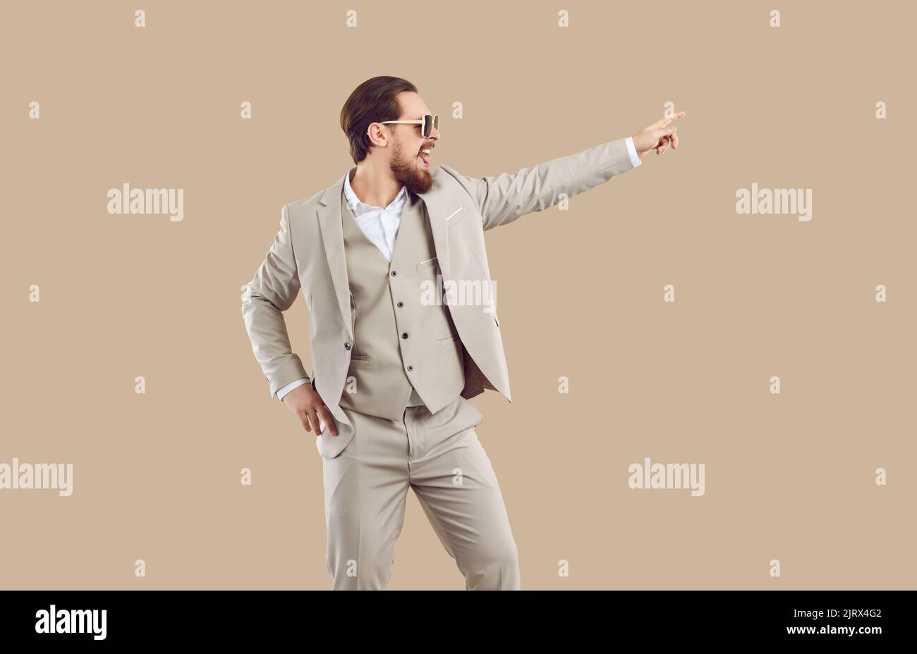 Funny excited young man in beige suit dancing and pointing his finger to right side Stock Photo