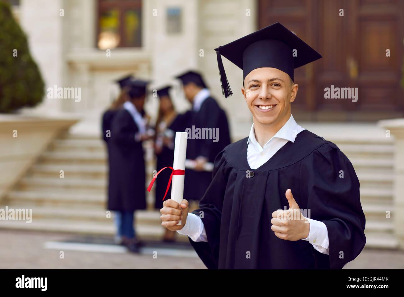 Portrait of joyful male university student with diploma who is doing excellent and approval sign. Stock Photo