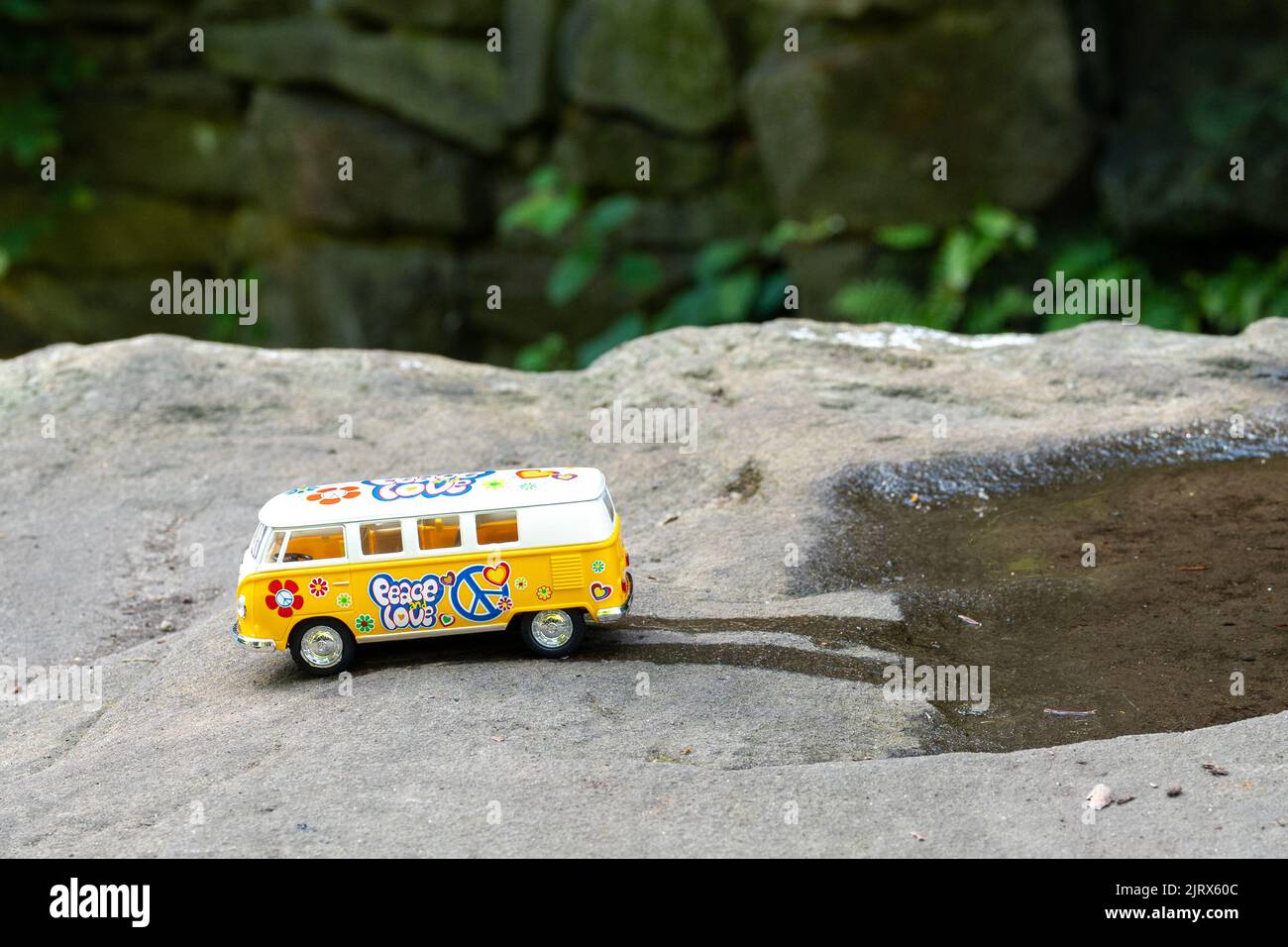 Yellow VW camper van model bus, in a nature scene, on a rock, driving out of a puddle of water. Stock Photo