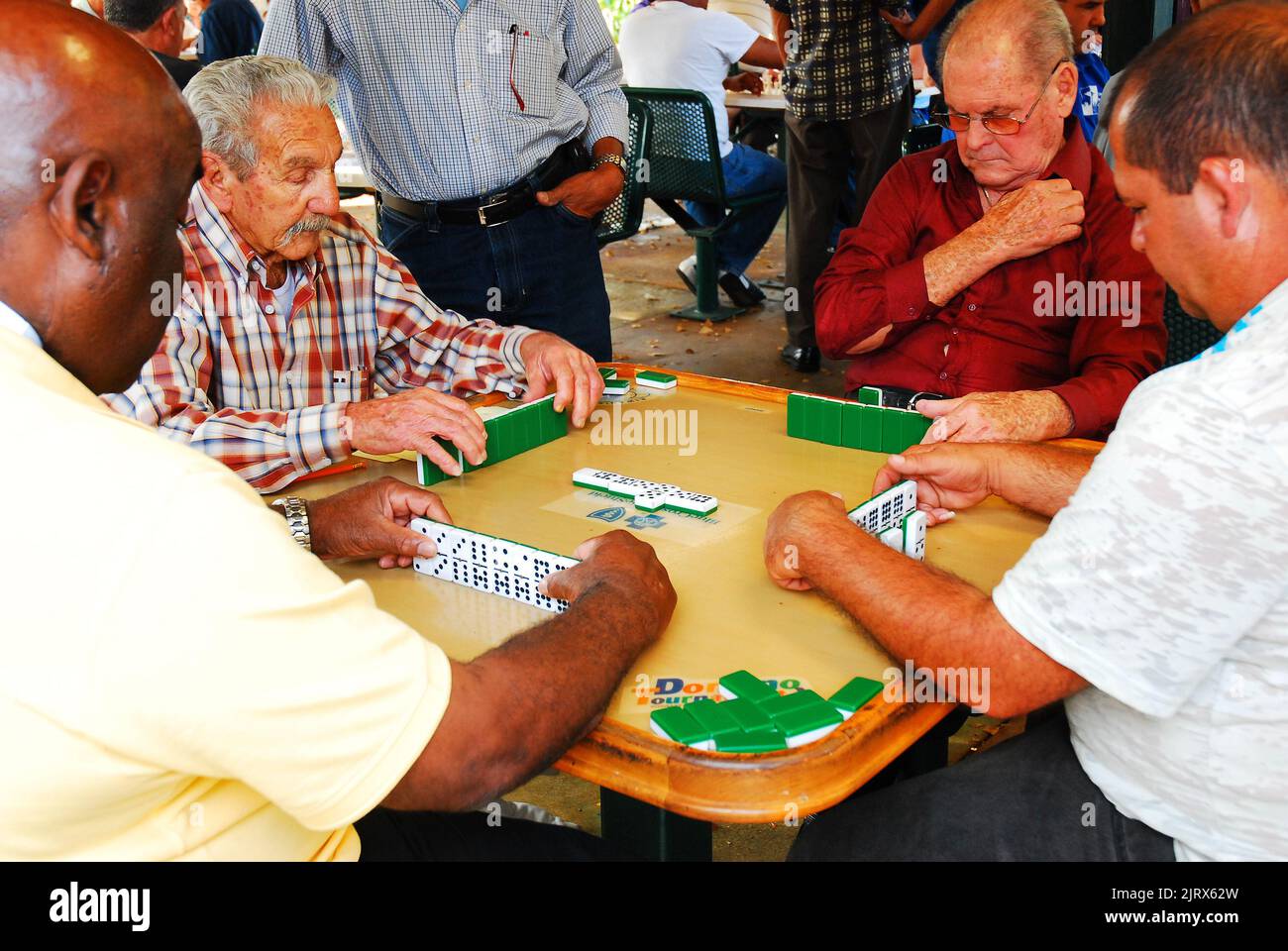 A group of senior men play a friendly game of dominos at a park in the Calle Ocho Cuban neighborhood of Miami Florida Stock Photo
