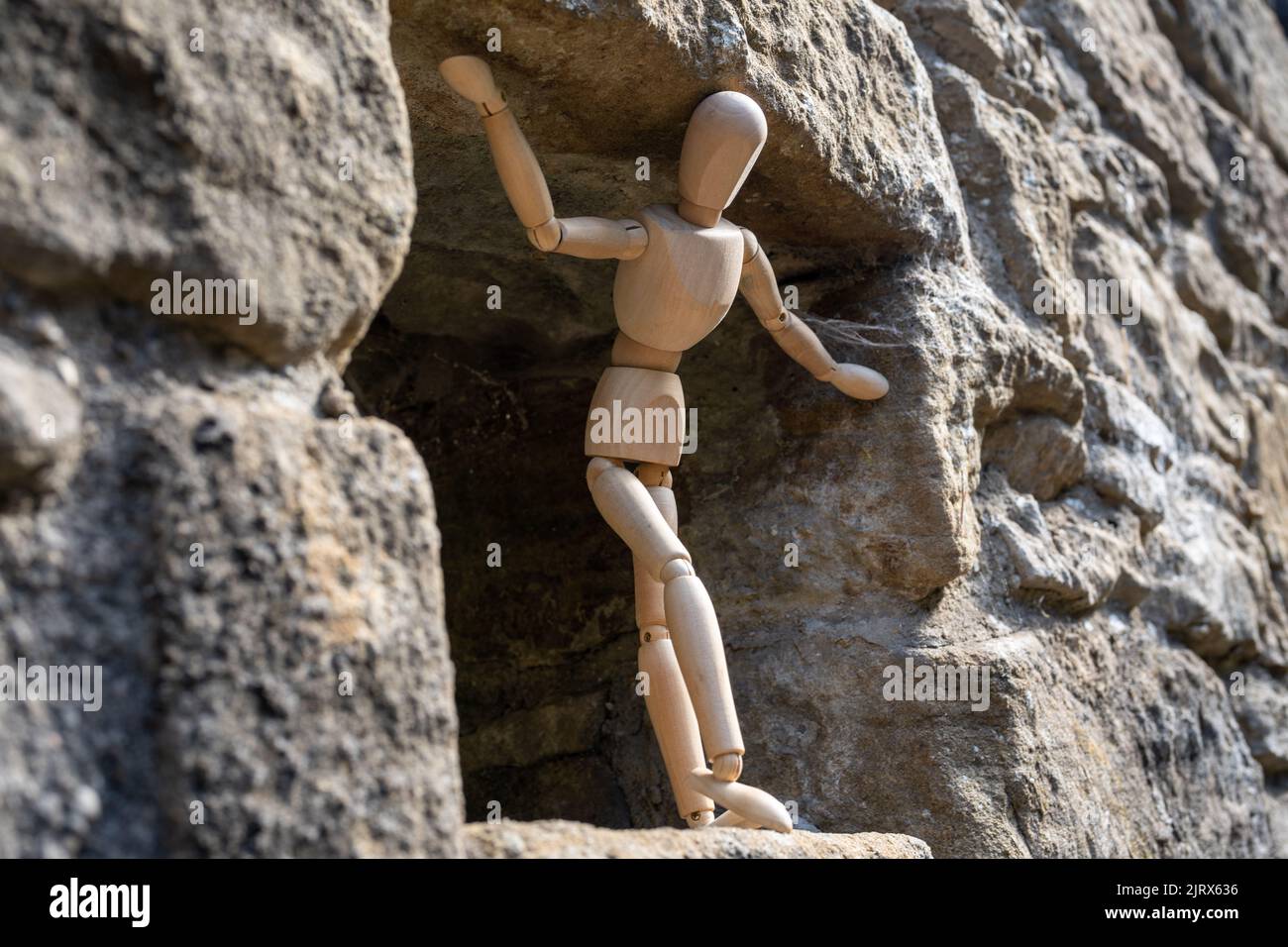 A wooden artist's figure standing, looking out of a stone building. Concept of an uncertain future, worry and concern. Stock Photo