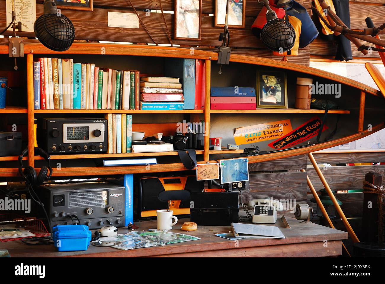 A radio and books are placed on shelves made out of an old canoe in the workplace office of an outdoor adventure tour company in California Stock Photo